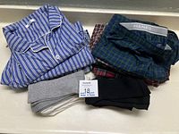 Folded blue and white striped men's pajama top with stacked plaid boxers and three pairs of socks in black, white, and gray