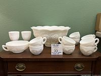 Full view of milk glass punch bowl set showing 6 cups, 2 goblets, handled dish, and large bowl with grape pattern.