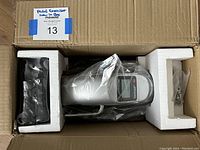 Top-down view of the pedal exerciser inside the box with foam protection showing the item wrapped in plastic and the digital screen visible.