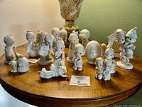15 Precious Moments figurines arranged on a wooden surface with a lamp in the background, showing each unique character and pose.