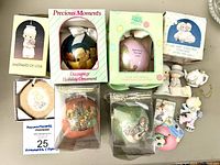 Lot of 12 Precious Moments ornaments shown with several in original boxes. The items include round baubles, figurines, and decoupage ornament in pastel colors.
