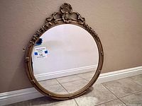 Full view of round mirror against a wall showing its gold ornate frame and shape.