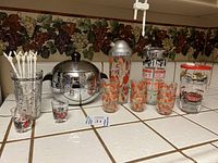 Full view of all barware items including shakers, ice bucket, various glasses placed on tiled surface with grapevine wallpaper background