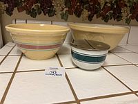 Set of four vintage ceramic bowls on white tiled counter, including cream bowls with and without decorative bands and a covered bowl with metal lid