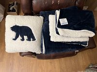 Top view of the folded navy blue and white sherpa comforter and off-white sherpa accent pillow with navy blue bear silhouette.
