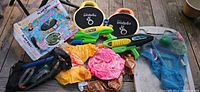 Lot laid out on wooden surface showing multiple beach toys: boxed Slam Ball game, floatation pads, water guns, snorkel gear, inflatables, mesh bag.