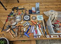 Overview of various scrap and hand tools laid out on wooden surface showing circular saw blades, clamps, mallets, pliers, screwdrivers and stapler.