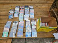 Photo showing a large assortment of CDs arranged on a wooden surface alongside a cardboard box containing more CDs.
