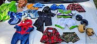 Assortment of Build-A-Bear clothes laid out on a white surface including costumes, shirts, shorts, and accessories.