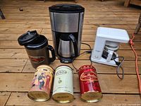 Two coffee makers, Tim Hortons mega mug, and three Tim Hortons collectible coffee containers shown on wooden surface.
