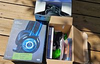 Photo showing boxed Afterglow wired headset with LED lighting, alongside open cardboard box containing three Microsoft wired controllers and several PC game discs in cases.