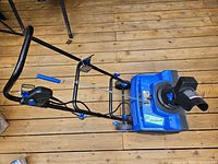 Full view of Snowjoe electric snowblower showing blue housing and black metal frame with two wheels on wooden floor