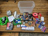 Overview of the entire lot arranged around a clear plastic bin showing various electrical tools, parts, wiring, tape, and outlet boxes.