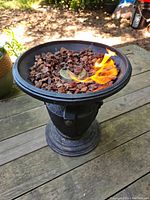 Propane fire bowl in use with flame and lava rocks, placed on wooden surface outdoors.
