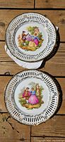 Two decorative German porcelain plates with pierced rims, each featuring a colorful romantic couple scene.