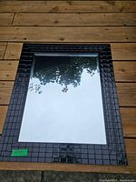 Front view of the rectangular mirror with a textured black frame and a reflective surface showing outdoor reflections.