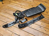 Top side view showing full sled with seat, steering wheel, and footrests on wooden deck