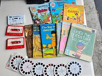 Lot laid out showing 7 children's books, 3 disney books on tape with red and white cassette tapes, and 6 View-Master disks.