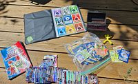 Photo showing Pokemon card binder with elemental energy cards in pockets, loose Pokemon cards in plastic bags, piles of assorted hockey cards, wooden box holder, and yellow card holder stand on wooden surface.