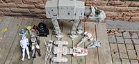 Wide shot displaying the AT-AT Walker, several action figures, and spaceships arranged on a wooden surface outdoors.