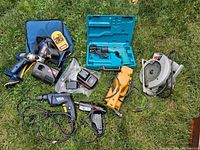 Overview of all tools on grass including drills, saw, planer, glue gun, chargers, batteries, laser level and cases