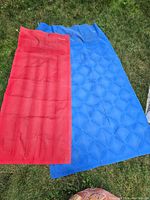Two vintage air mattresses, red and blue Barum brand, laid out on grass showing full mattress area.