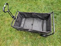Top view of empty black collapsible wagon with metal frame on grass.