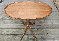 Full view of the older wooden fold-down table showing the pedestal base with three carved claw feet and the scalloped oval top.