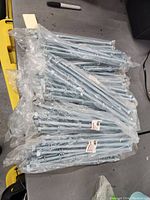 Pile of sealed plastic packages containing metal carriage bolts, showing quantity and size by visible labels and bolt heads.