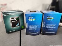 Photo of three processor boxes: one AMD Athlon II and two Intel Core i3 boxed processors.