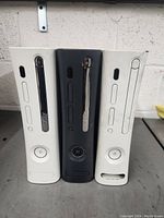 Front view of three Xbox 360 consoles including two white and one black unit showing disc drives and power buttons.
