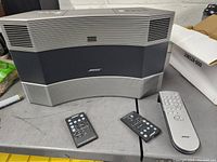 Gray Bose Acoustic Wave 2 Music System front view with three remotes placed next to the system on table.