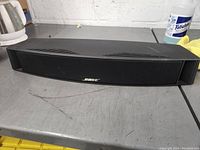 Front view of black Bose center channel speaker with fabric grille and silver Bose logo in center.