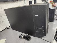 Front side view of the Bose subwoofer showing its rectangular shape, logo, and power cable on a workbench.