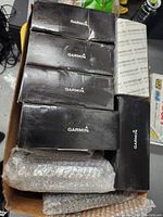 Cardboard box containing five black Garmin retail boxes, one white refurbished box and two bubble-wrapped units