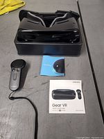 Samsung Gear VR headset placed on a stand with a controller and user manuals visible on a table surface.