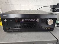 Full front view of Integra AV receiver showing the display, volume knob, buttons, and input ports on a metal surface.