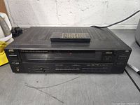 Front view of JVC RX-301 receiver with remote placed on top, showing tuning buttons and digital display lit.