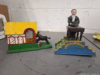 Photo showing both metal coin banks from the front, magician and cottage dog designs visible.