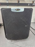 Front view of the subwoofer showing black mesh cover and silver Mirage logo plate with a green power indicator LED.