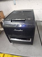 Front view of a black Swingline paper shredder showing the brand logo, control buttons, and power indicator light.