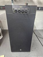 Front view of the Yamaha YST-SW205 subwoofer showing fabric speaker grill and top control panel with knobs and indicator lights.