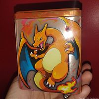 Front and right side of metal tin showing Charizard artwork with fiery background