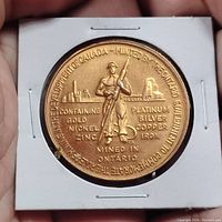 Front side of the coin showing miner holding a pickaxe with inscriptions about metals mined in Ontario.