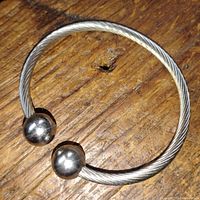 Steel magnetic balance bracelet photographed on wooden surface showing twisted wire design and two polished magnetic balls.