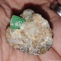 Close-up photo showing bright vivid green natural emerald crystal embedded in the host rock held in hand.