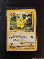 Clear photo of an original Jungle Set Pikachu Pokemon card showing details including 50 HP, Spark attack, weakness and retreat cost. The card is in a protective sleeve on a black background.