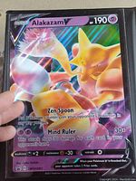 Front side of oversized holo foil Alakazam V Pokémon card showing character, attacks, HP, and other card details.