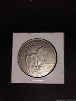 Reverse of US 1972 one dollar coin showing eagle landing on moon with olive branch and inscriptions.