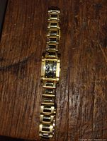 Photo of the full gold-tone Seiko wrist watch laid on a wood surface, showing the rectangular black dial and link bracelet.